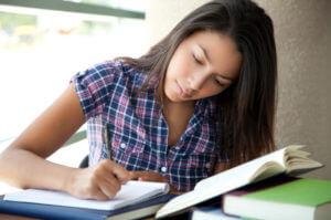 Girl doing homework, writing in a notebook with books and reading